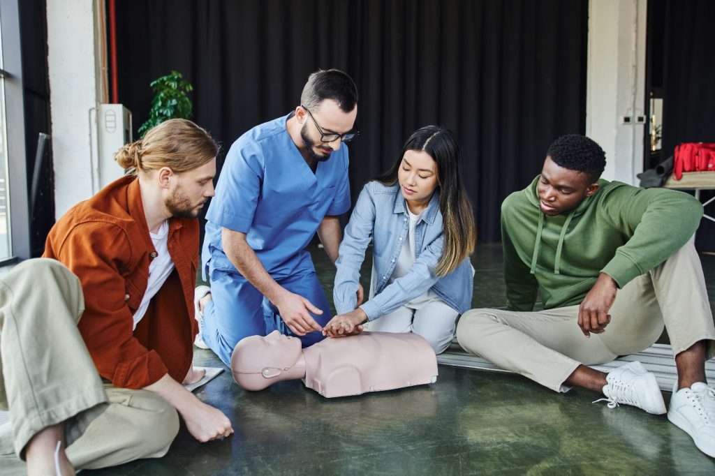 Betterdays Healthcare A diverse group of individuals attentively learns cpr techniques from an instructor on a dummy model during a first-aid training session.